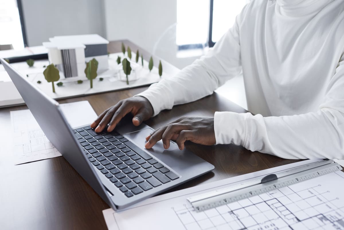 A man doing research on a laptop next to a model of a building and floorplan