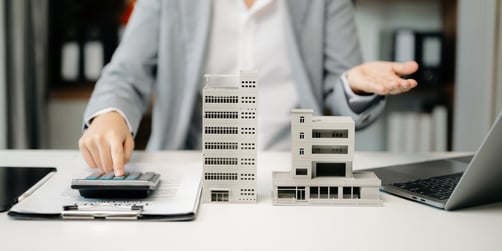 A woman sitting at a desk with models of commercial buildings and typing on a calculator