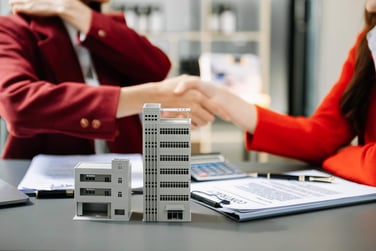 Two people shake hands over a commercial property lease next to commercial property model