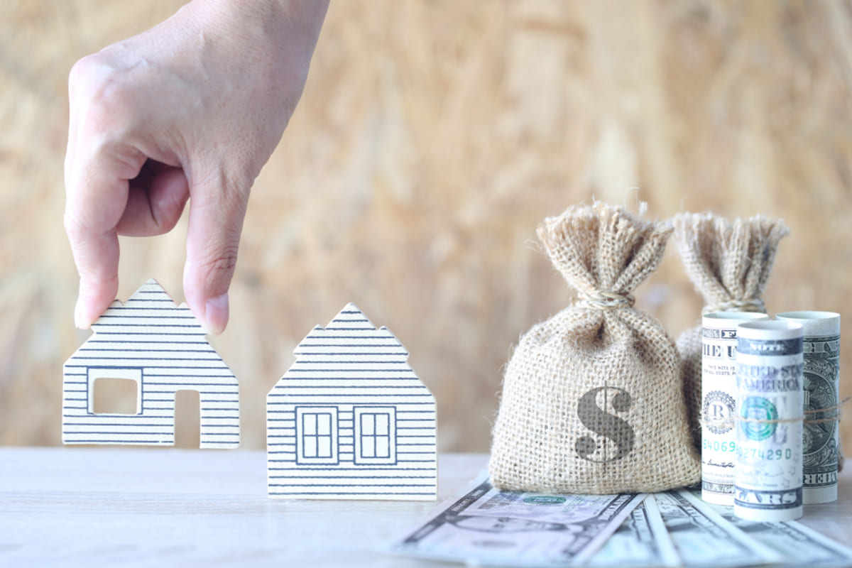 Money bag with banknote and woman hands holding model house on wooden background