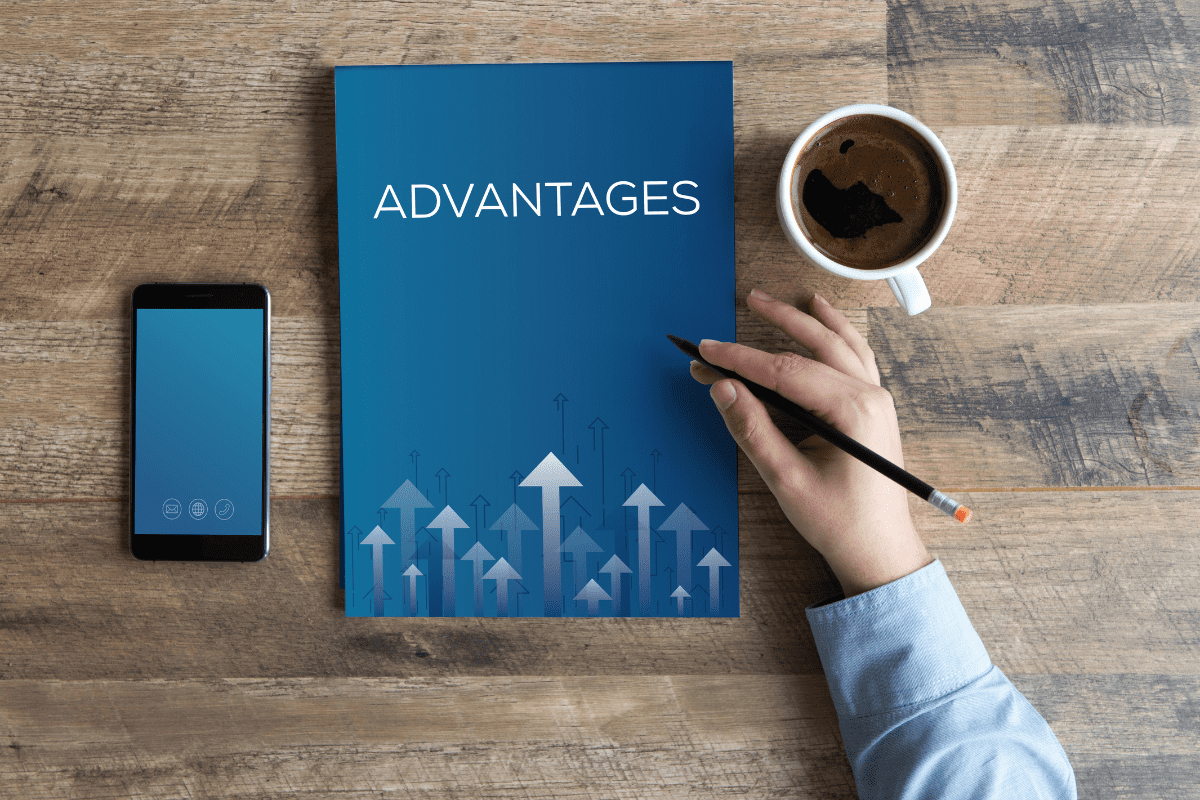 Notebook with the word ADVANTAGES written on cover page on desk with coffee, smartphone, and businessman’s hand