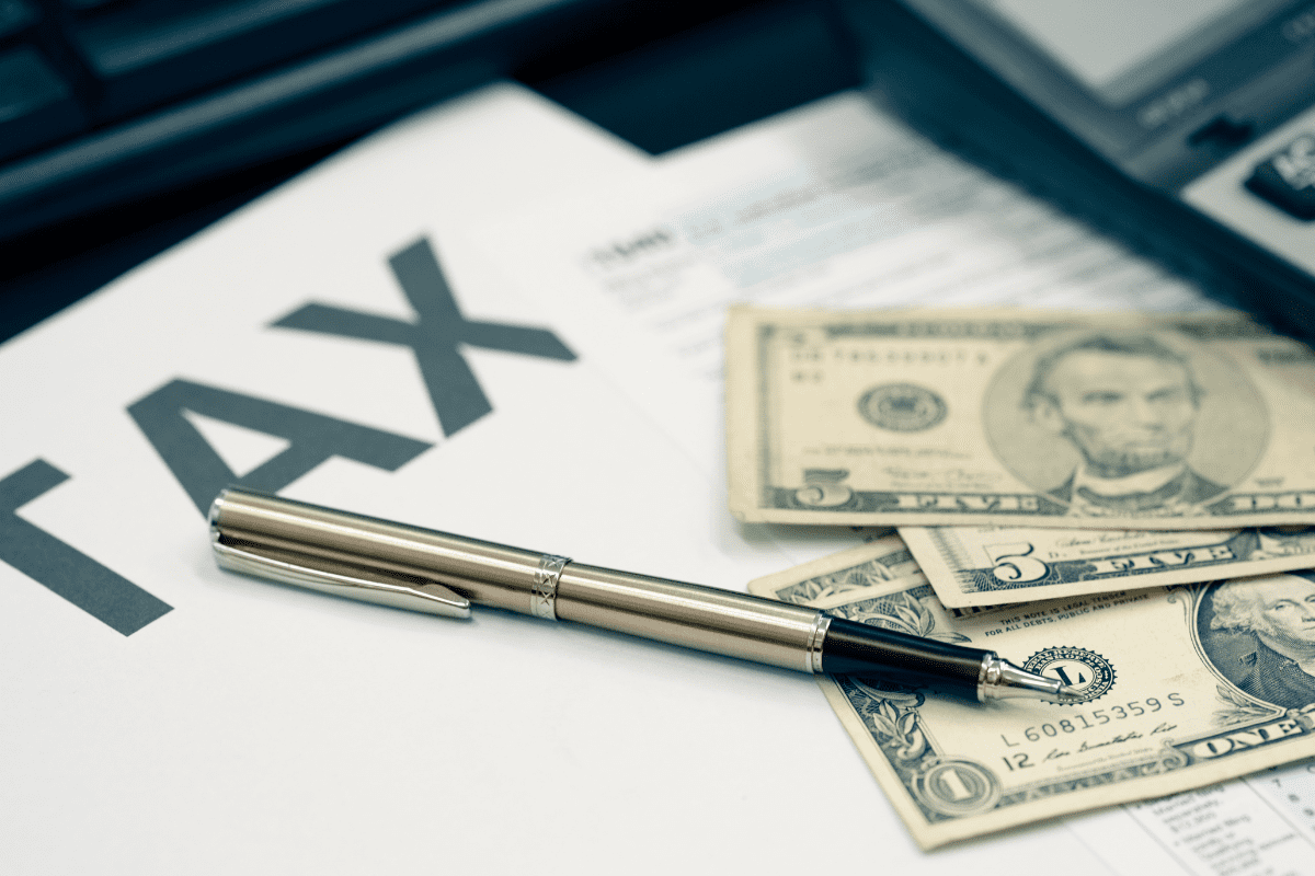 Paper with the word TAX on a desk with pen and dollar bills