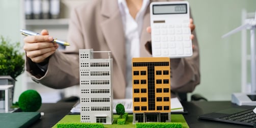 Someone pointing at models of commercial buildings and holding a calculator
