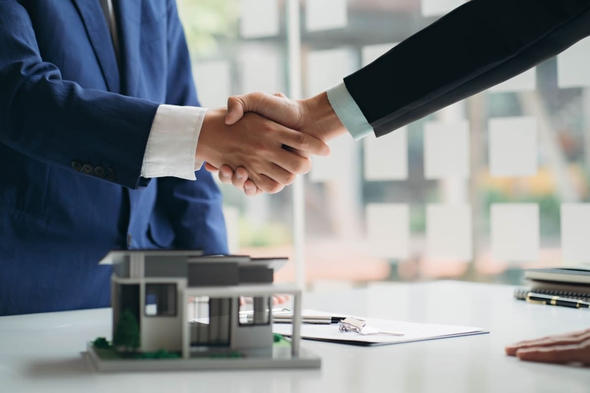 Two people shaking hands next to a model of a commercial building