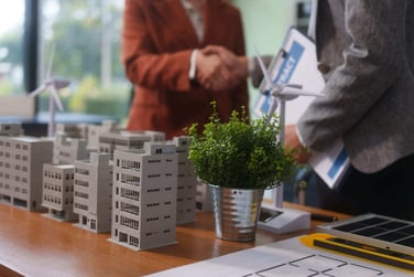 Two professionals shaking hands next to models of commercial real estate buildings.