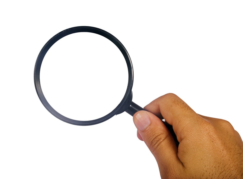 Close-up of hand holding magnifying glass, Kenwood Management insights into an investment loss autopsy concept. 