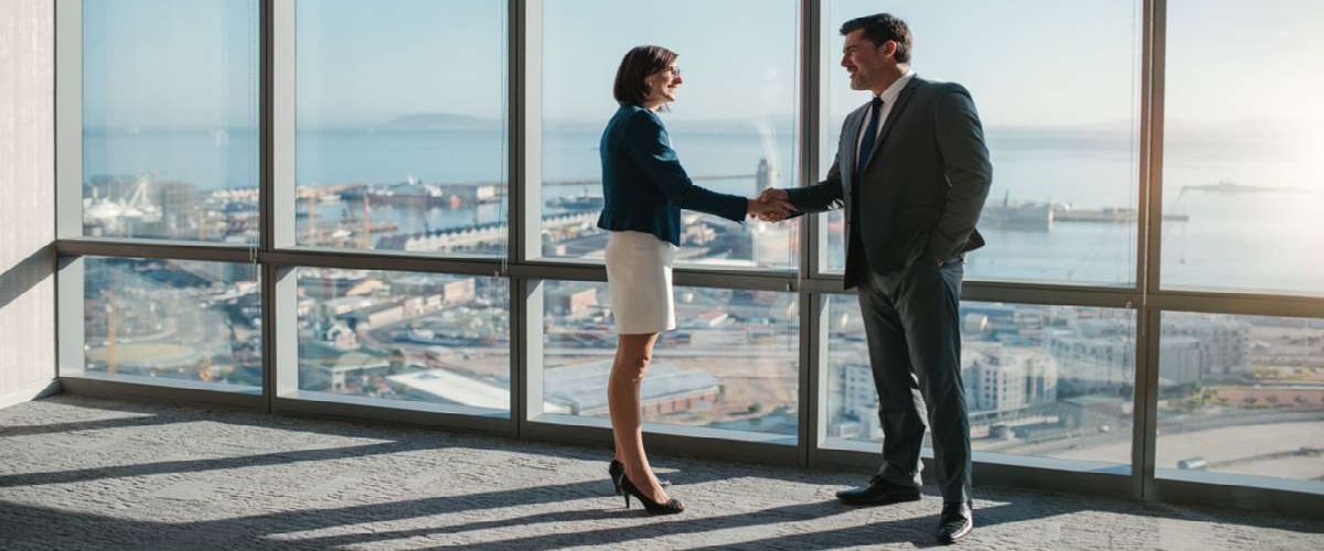 5 Businessman and businesswoman shaking hands together while standing in front of office building windows overlooking the city